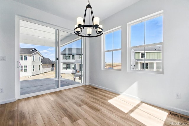 unfurnished dining area with visible vents, baseboards, an inviting chandelier, and wood finished floors