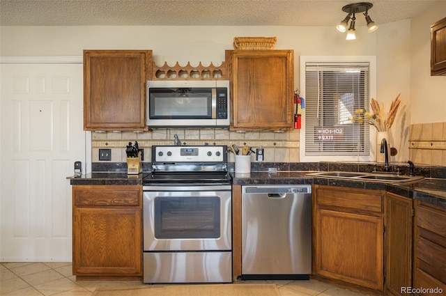 kitchen featuring backsplash, sink, a textured ceiling, light tile patterned flooring, and stainless steel appliances