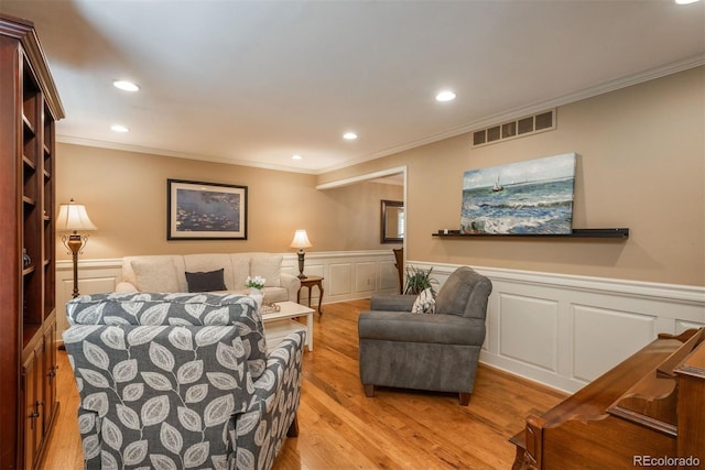 living area with a decorative wall, light wood-style floors, a wainscoted wall, visible vents, and ornamental molding