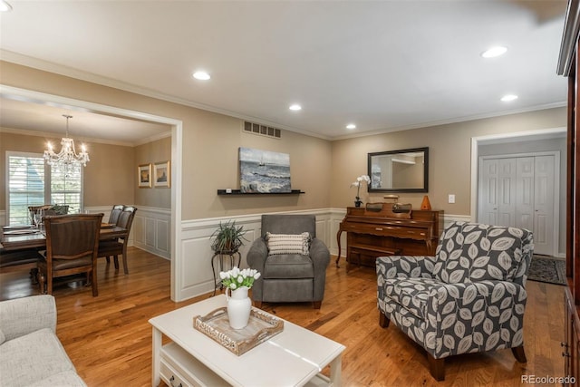 living room with visible vents, wainscoting, a chandelier, light wood-style floors, and ornamental molding