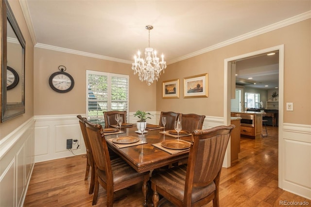 dining room featuring crown molding, wainscoting, wood finished floors, a chandelier, and a decorative wall