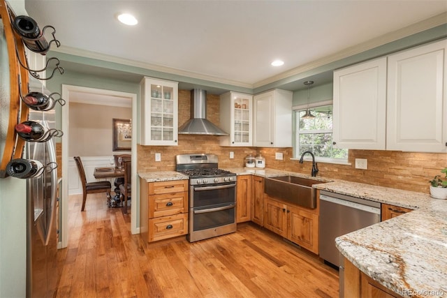kitchen featuring crown molding, wall chimney range hood, tasteful backsplash, a sink, and appliances with stainless steel finishes