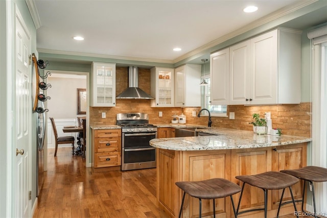 kitchen with wall chimney range hood, a sink, a peninsula, double oven range, and hardwood / wood-style flooring