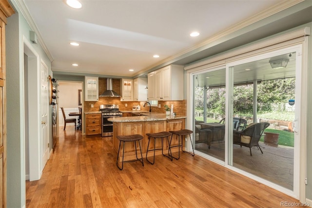 kitchen with crown molding, a peninsula, wall chimney range hood, range with two ovens, and a sink