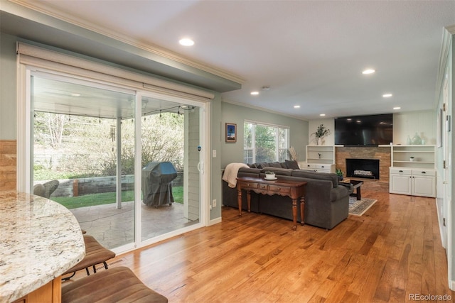 living area featuring crown molding, a fireplace, recessed lighting, and light wood-style flooring