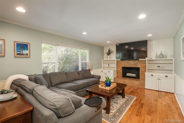 living room featuring crown molding, a fireplace with raised hearth, recessed lighting, and light wood-style flooring