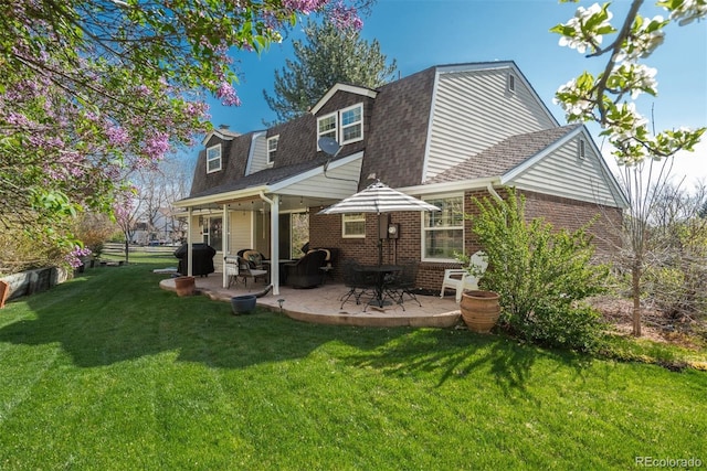 rear view of property with brick siding, a shingled roof, a patio area, and a yard