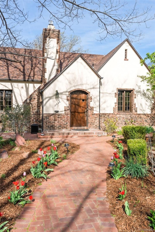 exterior space with brick siding, a chimney, central AC unit, and stucco siding