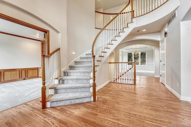 stairs with a notable chandelier, wood-type flooring, ornamental molding, and a high ceiling