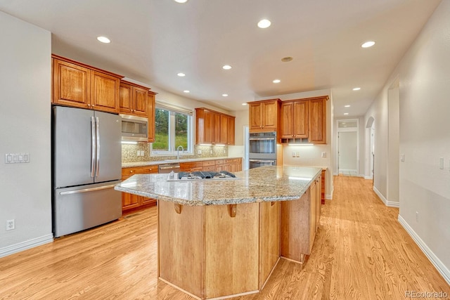 kitchen featuring a breakfast bar area, appliances with stainless steel finishes, light stone counters, light hardwood / wood-style floors, and a kitchen island