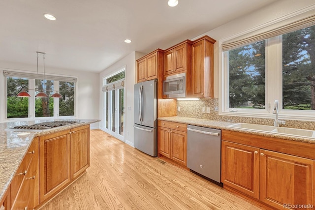 kitchen with sink, light stone counters, decorative light fixtures, light wood-type flooring, and appliances with stainless steel finishes