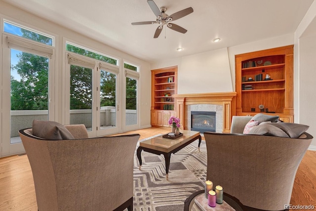 living room featuring a tiled fireplace, light hardwood / wood-style flooring, built in features, and ceiling fan