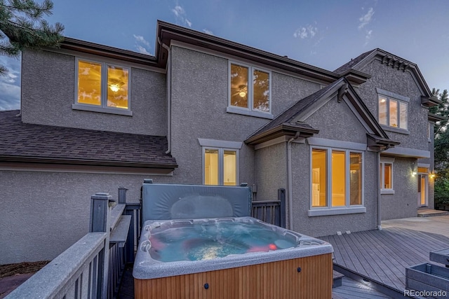 back house at dusk with a hot tub and a deck