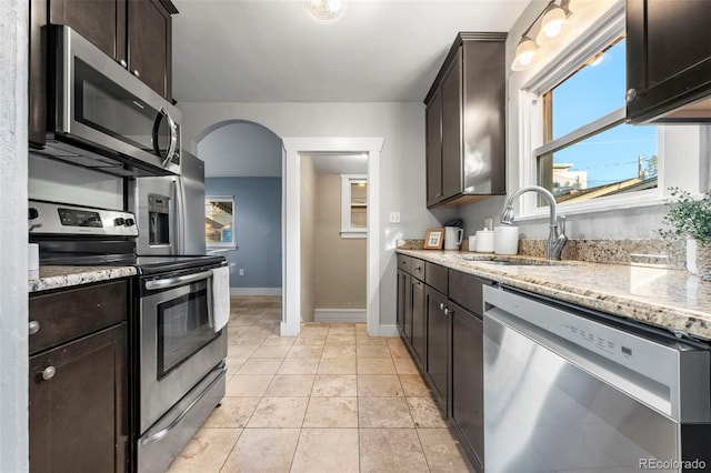 kitchen featuring sink, light tile patterned floors, dark brown cabinets, light stone counters, and stainless steel appliances