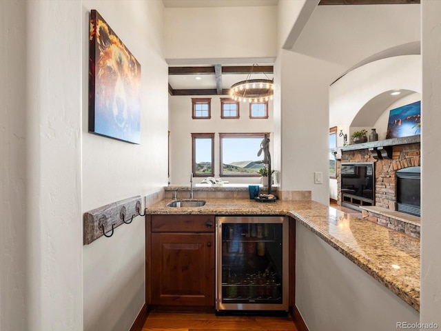 17121 Snow Creek Ln, Morrison, CO 80465 - indoor wet bar featuring beverage cooler, beamed ceiling, a stone fireplace, wood finished floors, and coffered ceiling