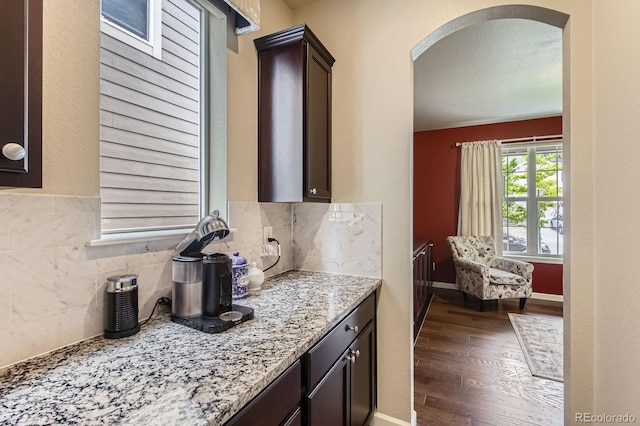 853 Jenny Ln, Berthoud, CO 80513 - kitchen with arched walkways, dark wood-type flooring, dark brown cabinetry, light stone countertops, and tasteful backsplash