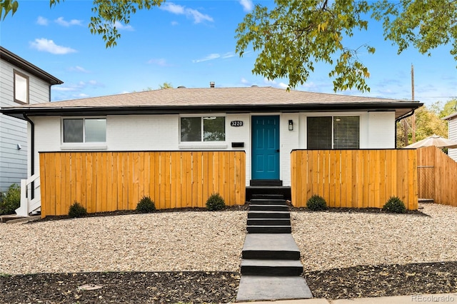 view of front of home with fence, a shingled roof, and brick siding