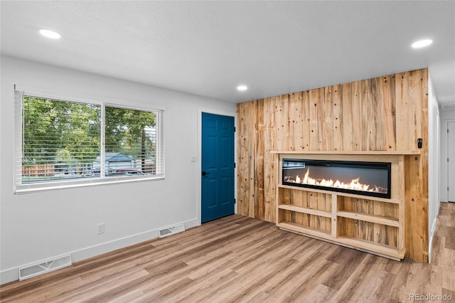 unfurnished living room with wood finished floors, a glass covered fireplace, recessed lighting, baseboards, and wood walls