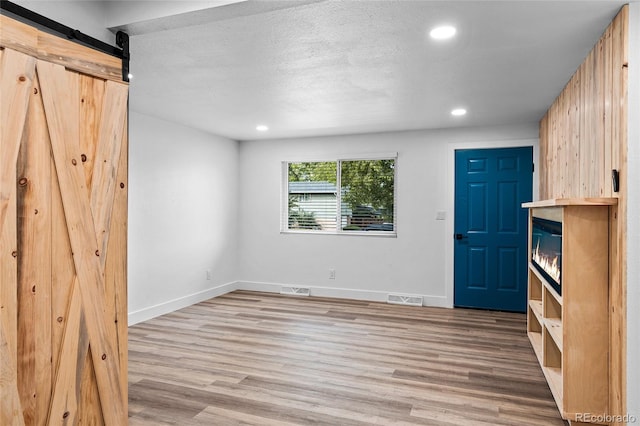 unfurnished room featuring recessed lighting, light wood-style flooring, a barn door, baseboards, and a textured ceiling