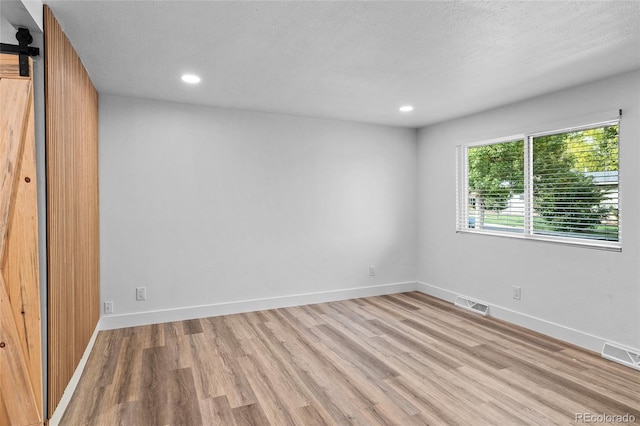 unfurnished bedroom with light wood-type flooring, a textured ceiling, recessed lighting, a barn door, and baseboards