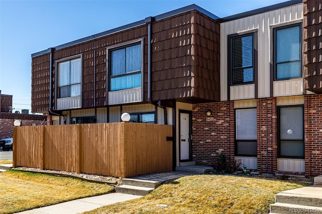 view of front of house featuring brick siding, mansard roof, and fence