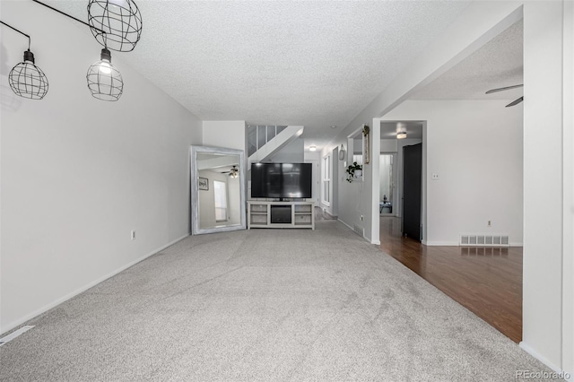 unfurnished living room with a ceiling fan, visible vents, and a textured ceiling