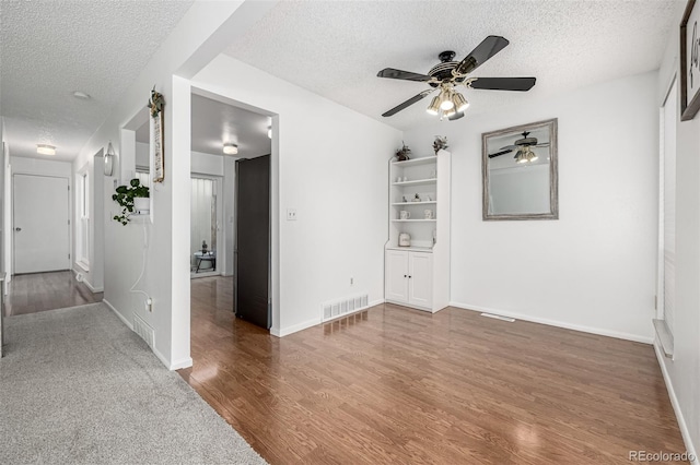 unfurnished room with visible vents, baseboards, wood finished floors, a textured ceiling, and a ceiling fan