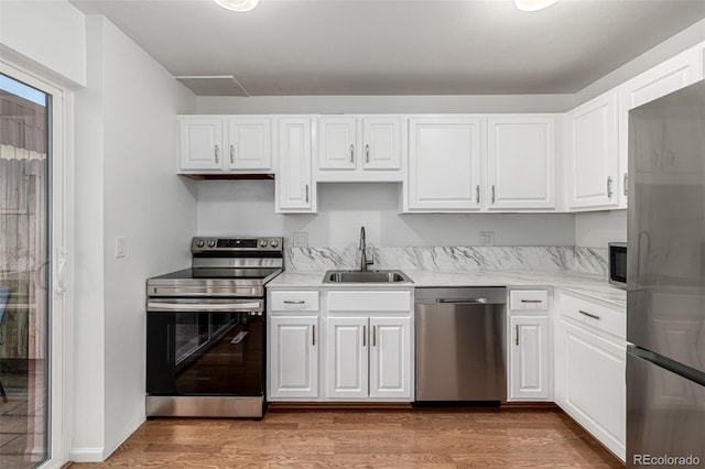 kitchen with light wood finished floors, a sink, white cabinetry, appliances with stainless steel finishes, and light countertops