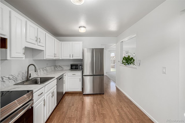 kitchen featuring baseboards, stainless steel appliances, wood finished floors, white cabinetry, and a sink