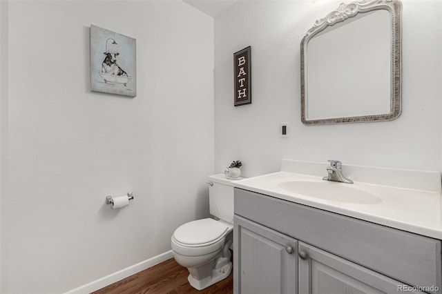 half bath featuring vanity, toilet, wood finished floors, and baseboards