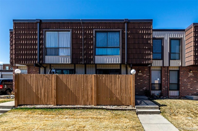 view of front of home featuring mansard roof, brick siding, a front lawn, and fence