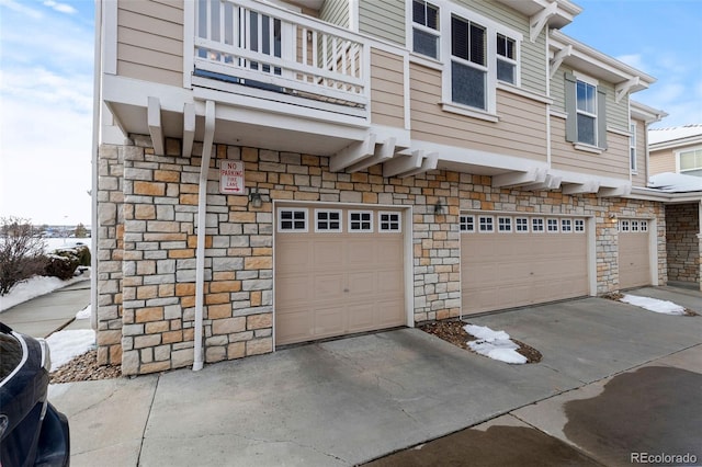 exterior space featuring a garage, stone siding, driveway, and a balcony