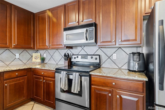 kitchen with appliances with stainless steel finishes, backsplash, light stone counters, and brown cabinets