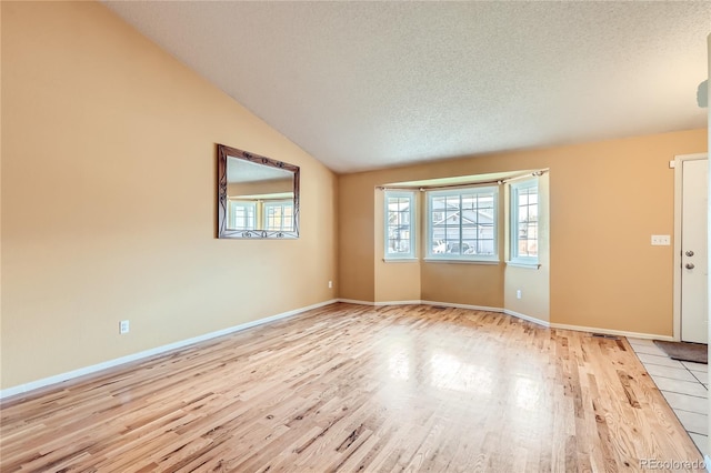 spare room featuring a textured ceiling, lofted ceiling, and light hardwood / wood-style flooring