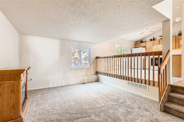 unfurnished room featuring a textured ceiling, carpet flooring, and lofted ceiling