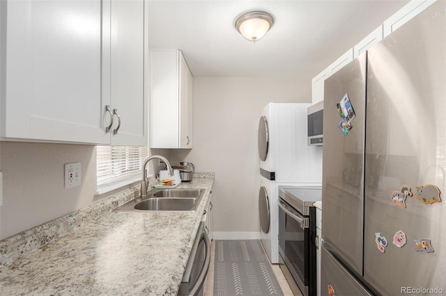 kitchen featuring stacked washer / dryer, baseboards, a sink, white cabinetry, and stainless steel appliances