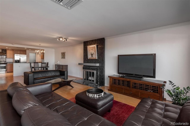 living room featuring a fireplace, hardwood / wood-style floors, ornamental molding, and an inviting chandelier