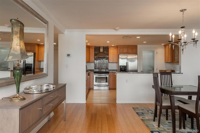 kitchen with wall chimney range hood, pendant lighting, light hardwood / wood-style floors, crown molding, and stainless steel appliances