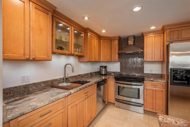 kitchen featuring wall chimney exhaust hood, stainless steel appliances, dark stone countertops, sink, and light tile patterned floors