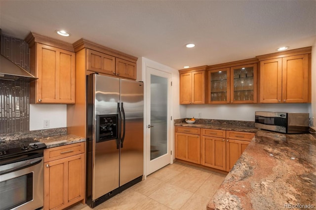 kitchen with stainless steel appliances, dark stone countertops, and wall chimney range hood