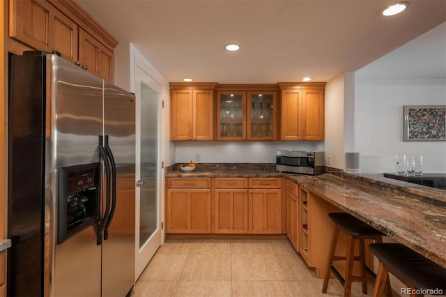 kitchen with stainless steel appliances, dark stone countertops, ornamental molding, a breakfast bar, and light tile patterned floors