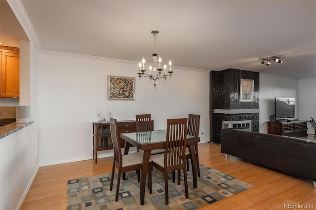 dining space with a fireplace, a notable chandelier, ornamental molding, and light hardwood / wood-style floors