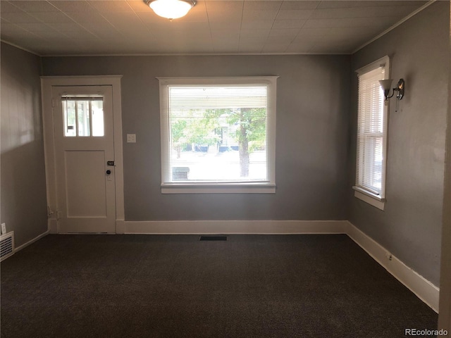 foyer with crown molding, baseboards, dark colored carpet, and visible vents