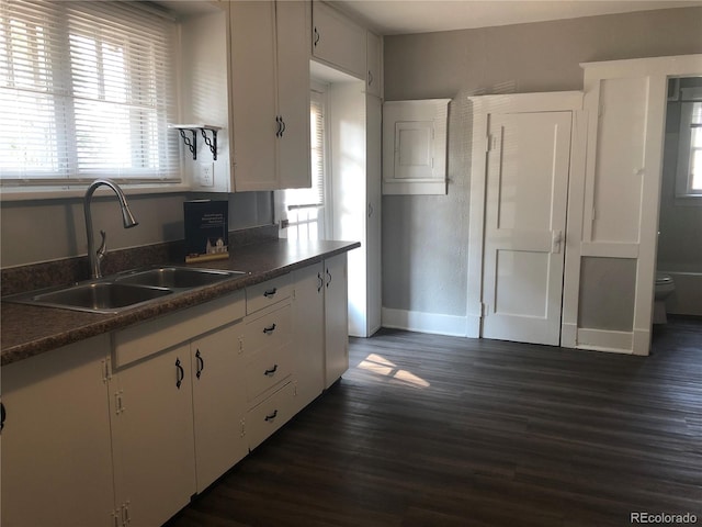kitchen with a sink, dark countertops, white cabinets, baseboards, and dark wood-style flooring