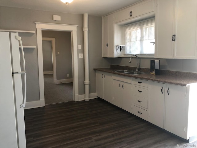 kitchen featuring dark countertops, dark wood finished floors, freestanding refrigerator, white cabinetry, and a sink