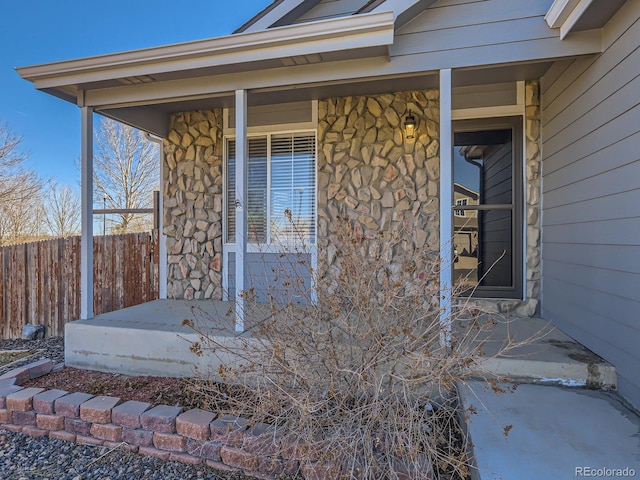 property entrance with covered porch, stone siding, and fence