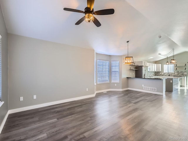 unfurnished living room featuring dark wood-type flooring, visible vents, vaulted ceiling, and baseboards