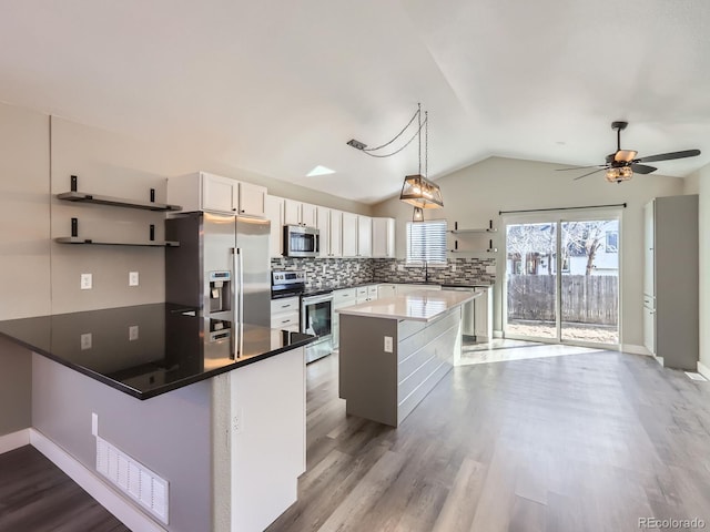 kitchen featuring wood finished floors, a peninsula, vaulted ceiling, stainless steel appliances, and backsplash