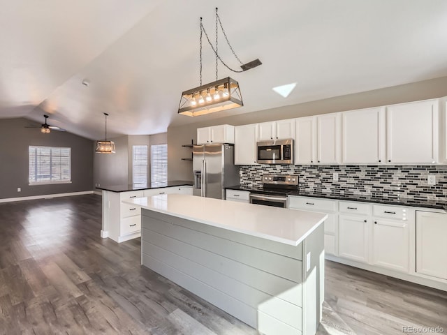 kitchen with dark wood-style flooring, stainless steel appliances, dark countertops, backsplash, and vaulted ceiling