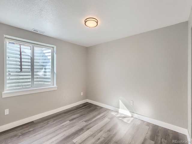 spare room with visible vents, a textured ceiling, baseboards, and wood finished floors
